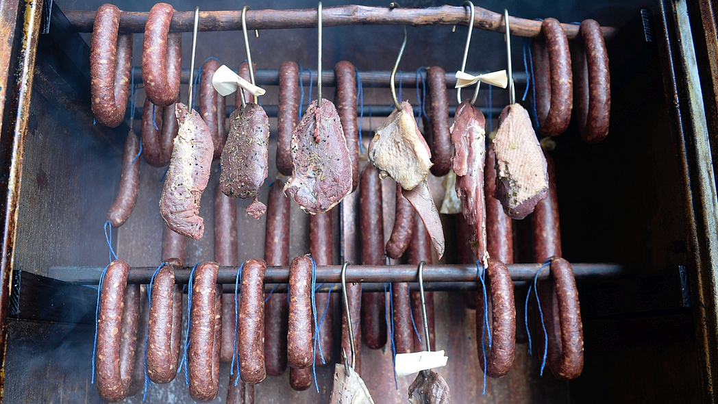Würste und Teilstücke von Wildfleisch hängen im Räucherschrank
